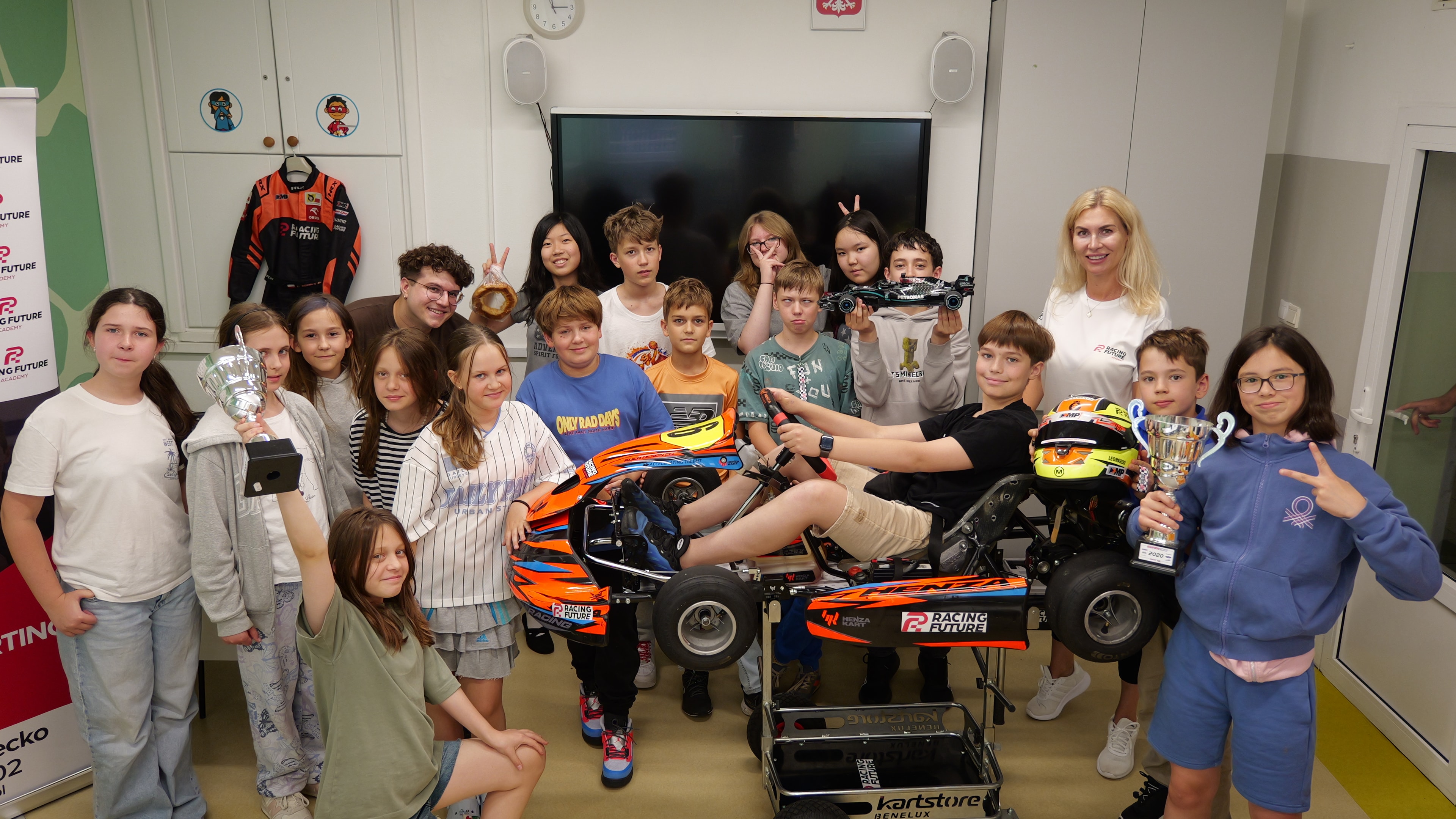Young Racing Future participants with their instructor, trophies, and a go-kart